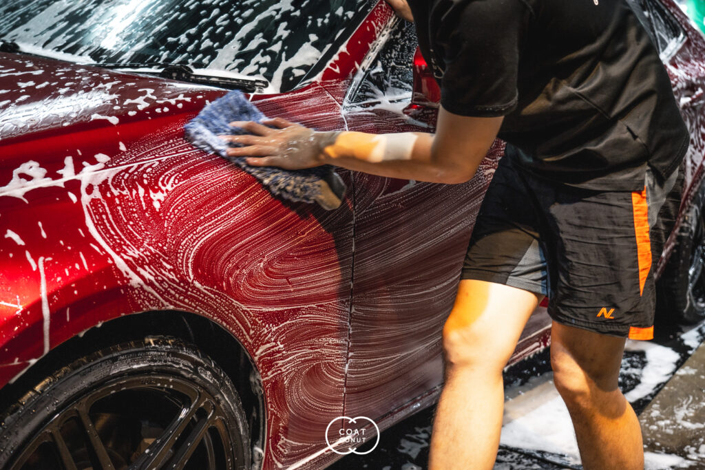 Detailer hand washing a red car with a microfiber mitt and foam swirls