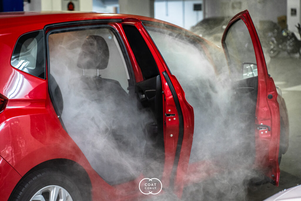 Interior steam cleaning in progress on a red car, doors open and filled with steam