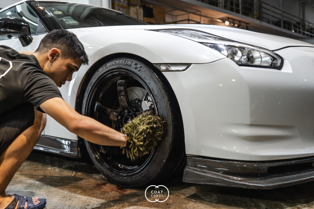 Detailer hand washing the black wheel of a white sports car with a mitt