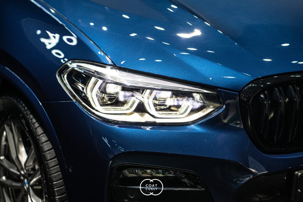 Blue BMW front quarter with lit LED headlights under studio lighting